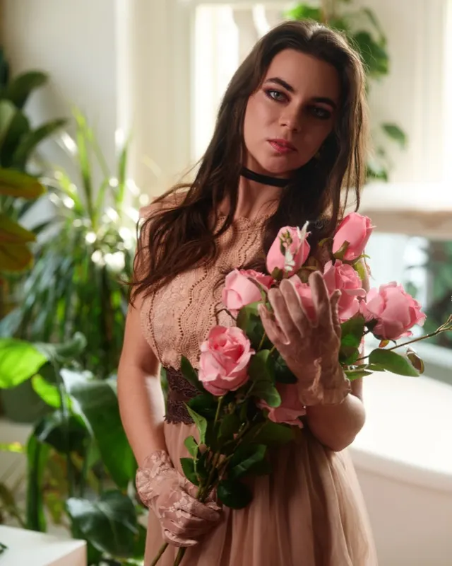 Milena in beige dress holding pink roses among green plants, portrait session Wroclaw