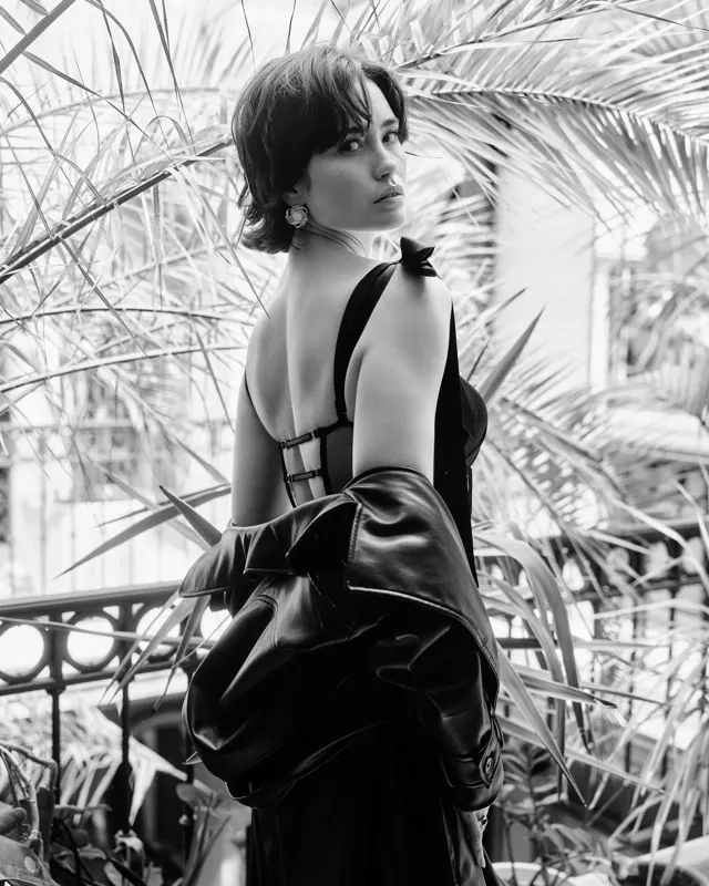 Black and white portrait of Nikola with open back among palms in orangery, portrait session Warsaw