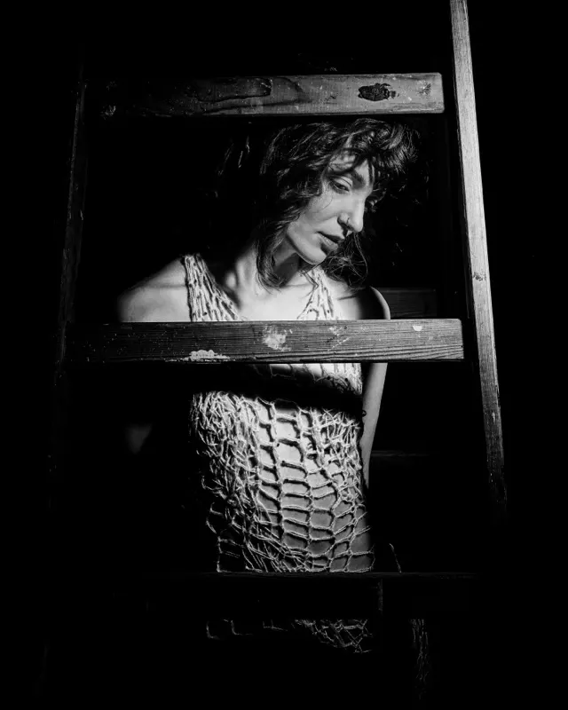 Black and white portrait of Paulina in mesh top behind a ladder, artistic session Wrocław