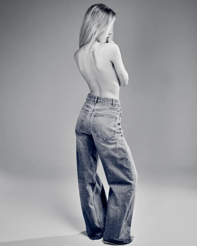 Karolina w szerokich jeansach odwrócona tyłem, czarno-biały portret studyjny z odkrytymi plecami
